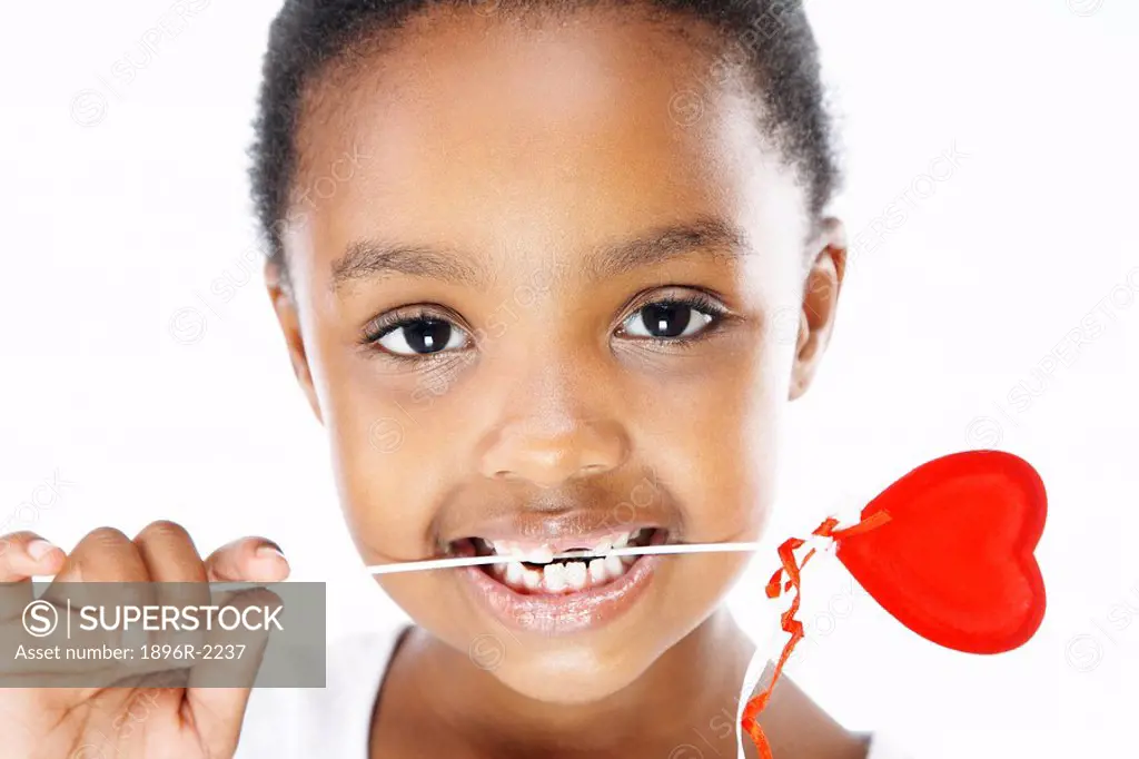 Young girl holding heart lollipop in her teeth