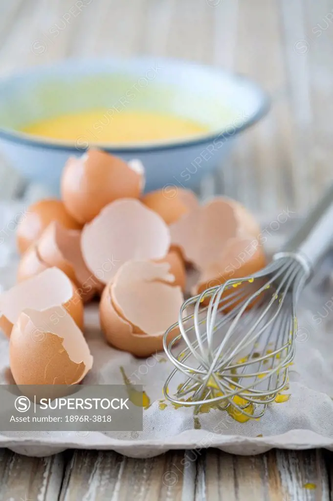 Egg Shells and Whisk on an Egg Tray with Beaten Eggs in a Bowl in the Background  Studio Shot