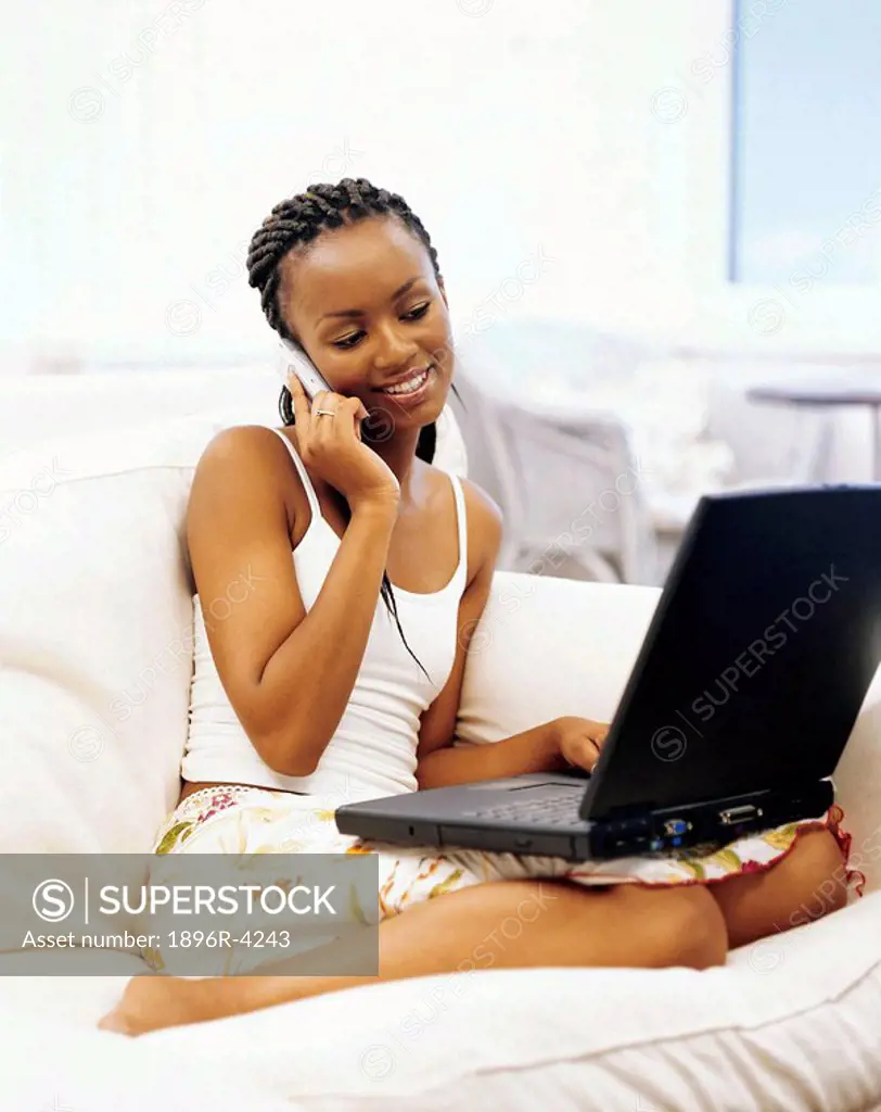 Young African Woman on a Cell Phone, Holding a Laptop Computer  Cape Town, Western Cape Province, South Africa