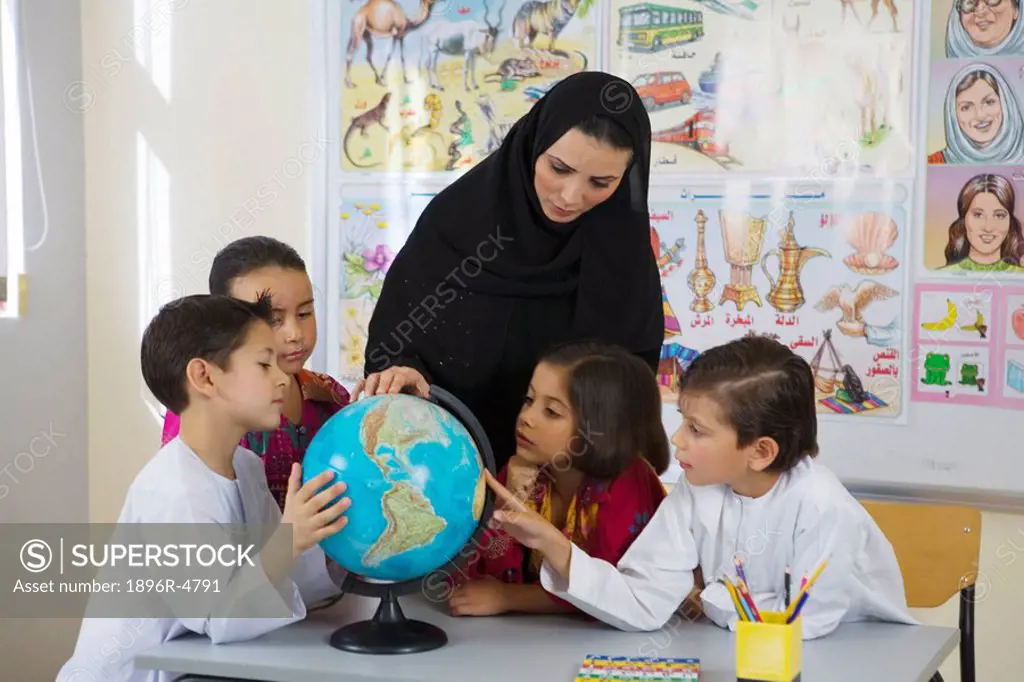 Group of students and teacher looking at globe in classroom