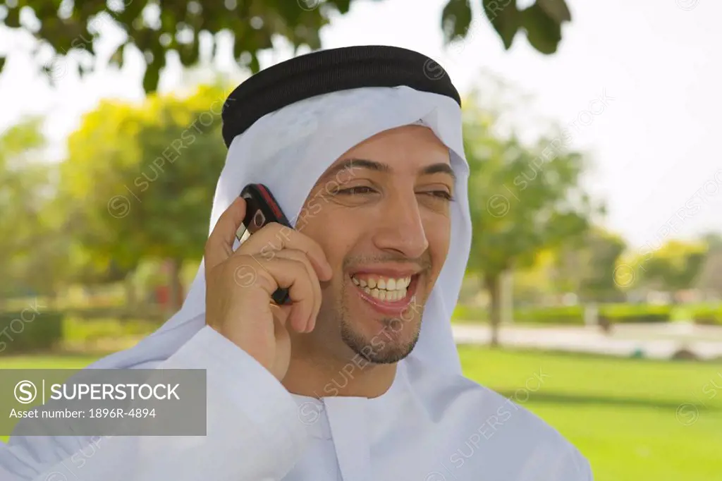 Laughing Arab Man on Mobile Phone in Park, Facing Camera  Dubai, United Arab Emirates