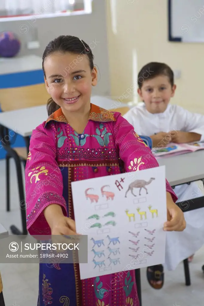 Smiling Girl Holding Homework in Classroom, Front View  Dubai, United Arab Emirates