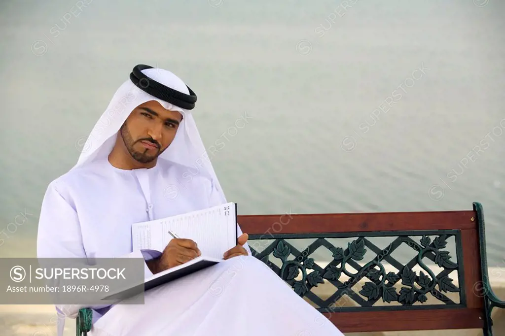 Arab Man Sitting on Park Bench Writing Journal  Dubai, United Arab Emirates