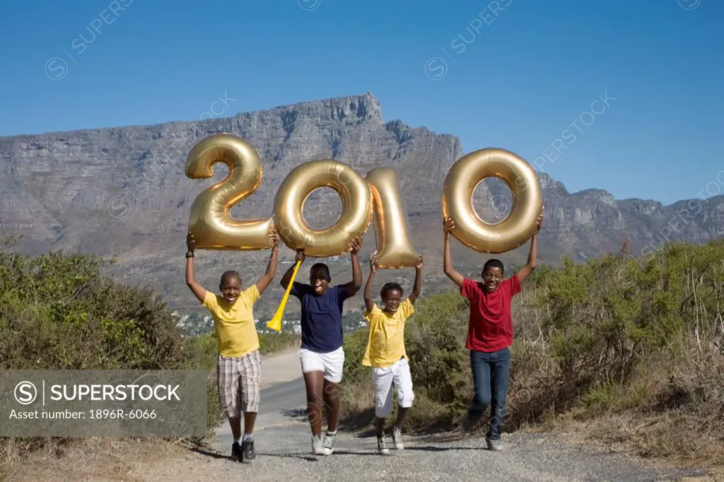 Jumping boys holding balloons shaped in numbers 2010, with South African flag, Table Mountain in background, Cape Town, Western Cape Province, South A...