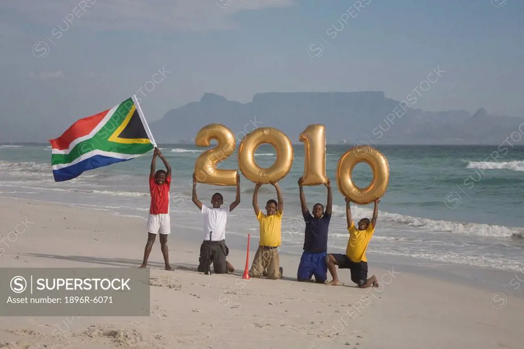 Young boys on beach, holding South African flag and golden balloons with numbers 2010, Table Mountain in background, Blouberg Beach, Cape Town, Wester...