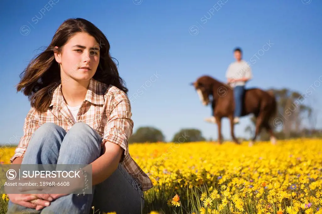 Woman in foreground with man on a horse in the background in a field of Namaqualand flowers. Nieuwoudtville, Northern Cape Province, South Africa
