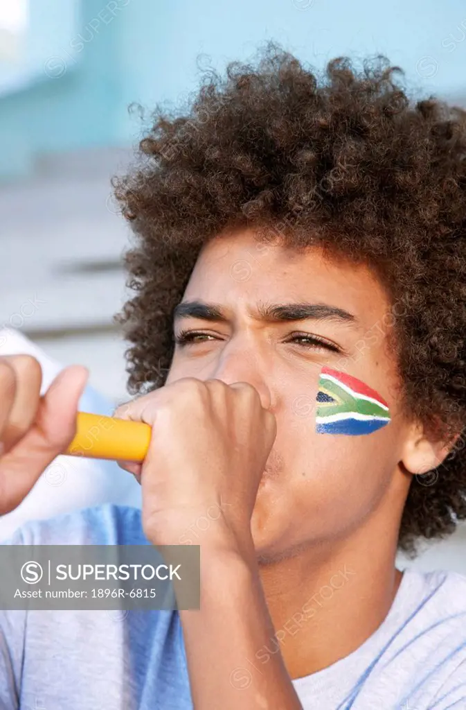 Sports fan with South African flag painted on his cheek blowing a vuvuzela. Cape Town, Western Cape Province, South Africa