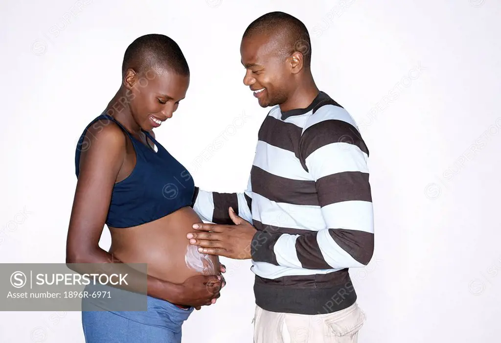 Man moisturising pregnant woman´s stomach. Studio Shot.