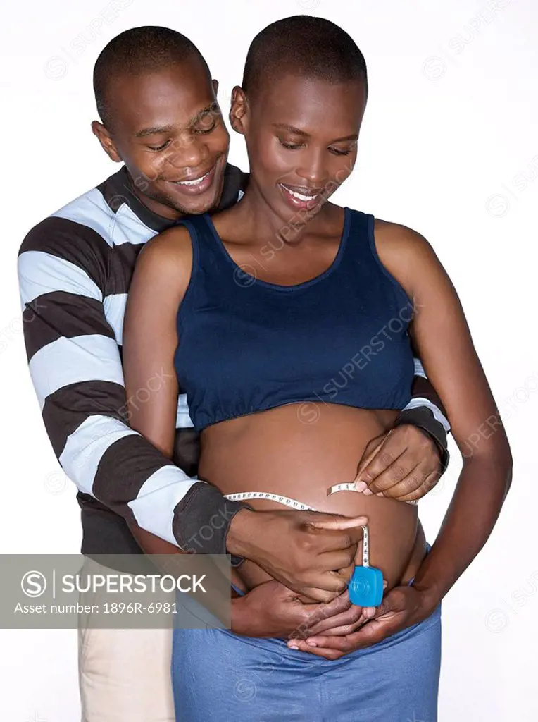 High angle view of pregnant woman and partner measuring her tummy. Studio Shot.