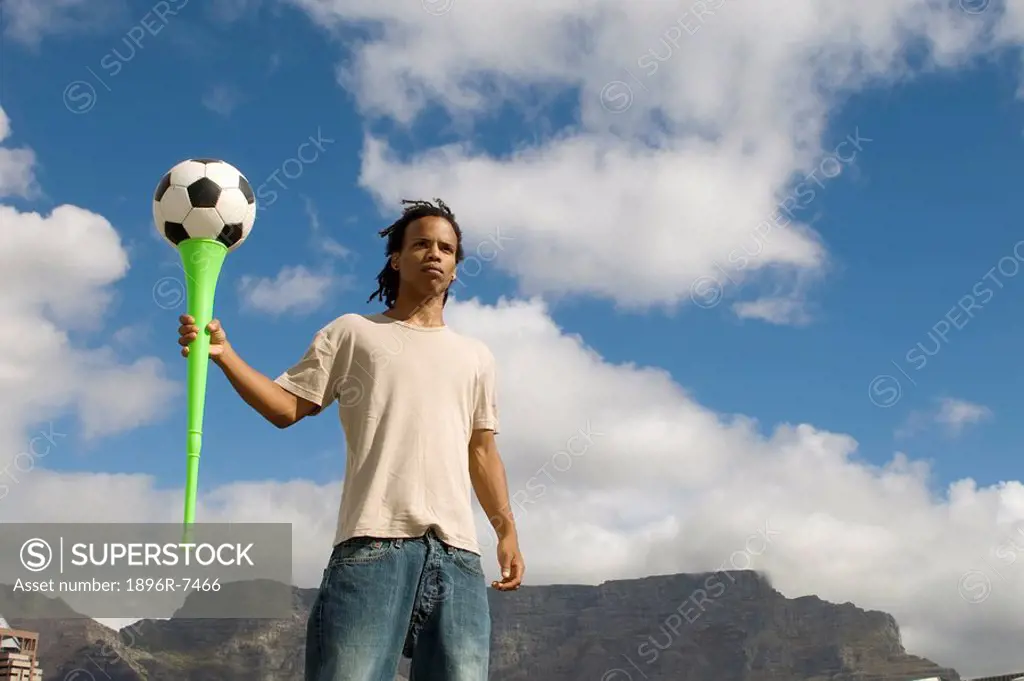 Young football fan holding football on top of a vuvuzela, Table Mountain in background. Cape Town, Western Cape Province, South Africa.