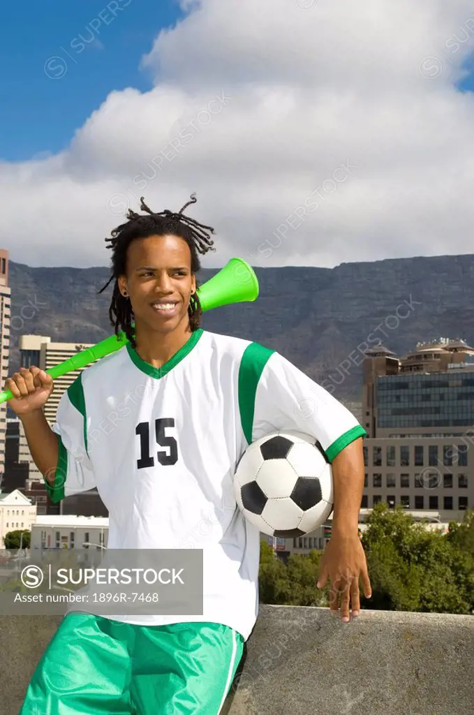 Young soccer player sitting on wall holding soccer ball and vuvuzela, Table Mountain in background, Table View, Cape Town, Western Cape Province, Sout...