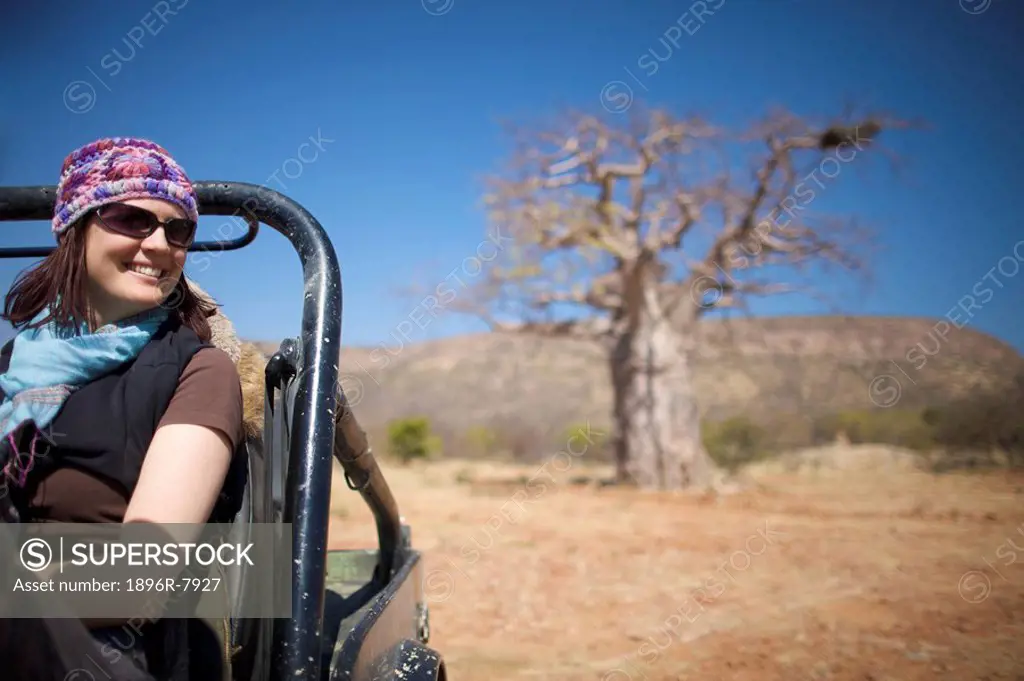Young woman sitting in motor vehicle with Baobab tree in background, Kunene river area, Kaokoland, Namibia