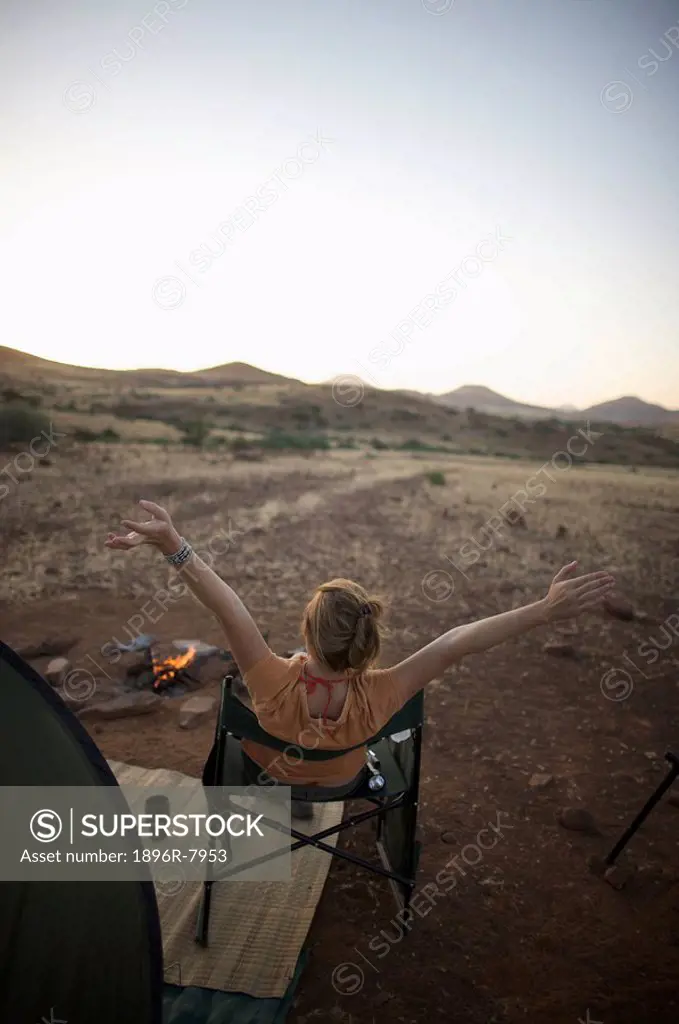 Rear view of woman at sunset at camp fire with arms in the air, Sesfontein, Kaokoland, Namibia