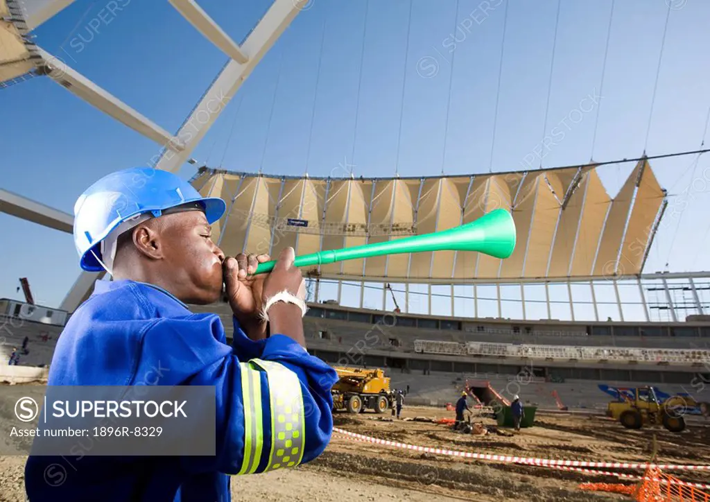 Construction worker blowing vuvumzela in front of construction work, Moses Mabhida Stadium, Durban, KwaZului_Natal Province, South Africa