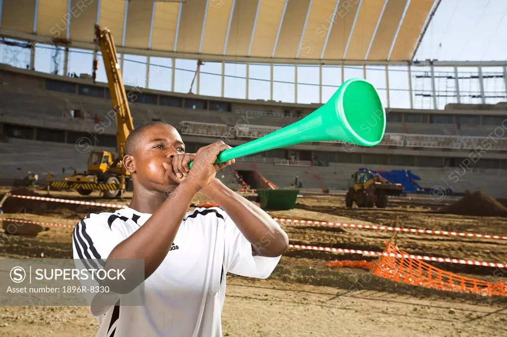 Football player blowing vuvumzela in front of construction work, Moses Mabhida Stadium, Durban, KwaZului_Natal Province, South Africa