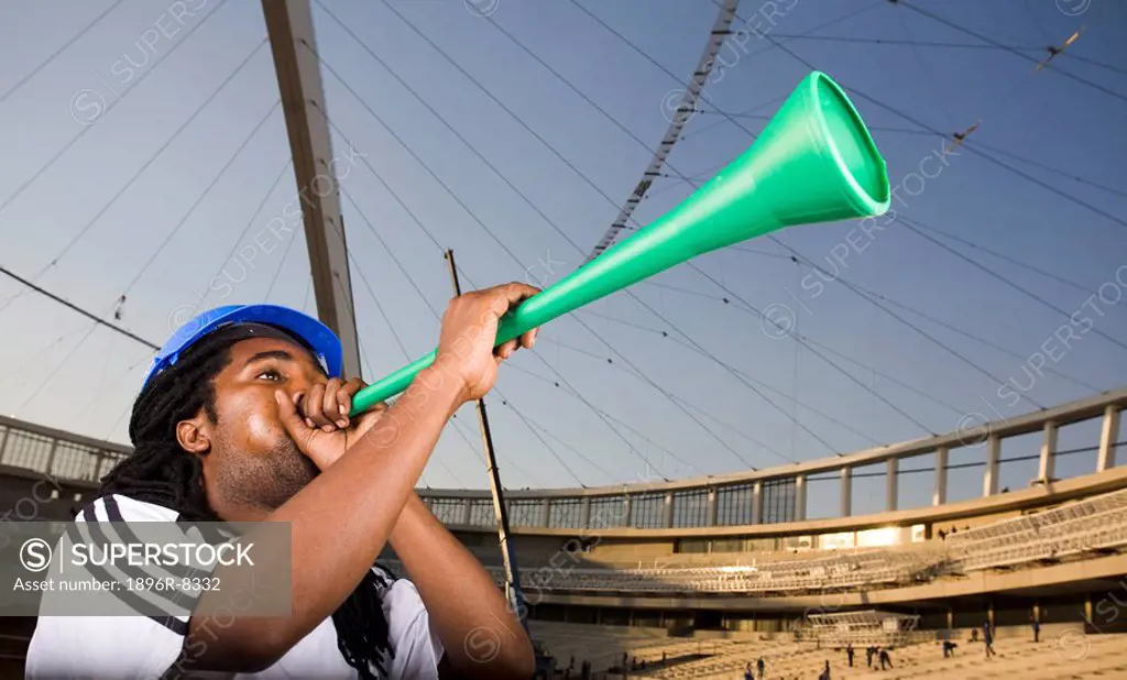 Construction worker wearing soccer outfit and blowing vuvuzela in front of Construction work, Moses Mabhida Stadium, Durban, KwaZului_Natal Province, ...