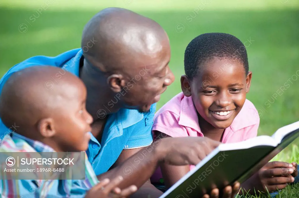 Father reading with children 4_8 on lawn in garden, Johannesburg, Gauteng Province, South Africa