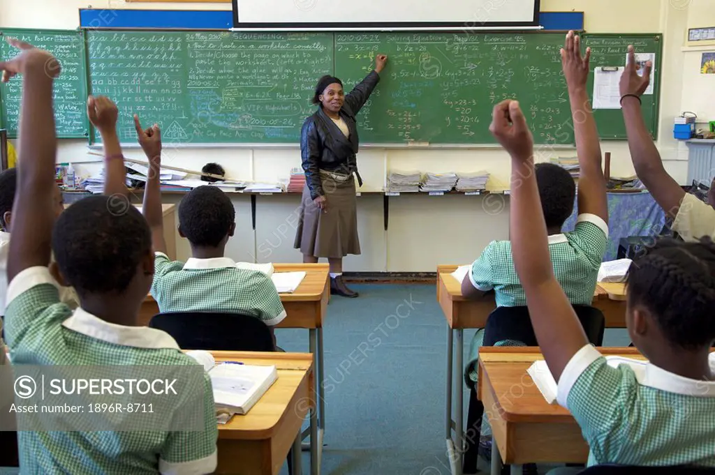 View of a full classroom of pupils with their hands raised, looking toward teacher, KwaZulu Natal Province, South Africa