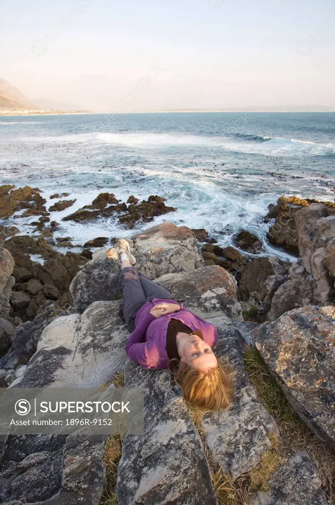 Mid adult woman laying on rocky shore, Hermanus, Western Cape Province, South Africa