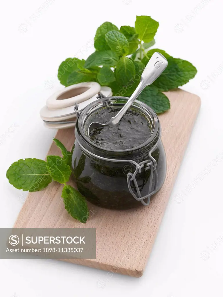 A jar of mint sauce with a spoon and fresh leaves