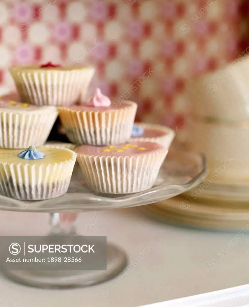 A detail of iced fairy cakes on a glass cake stand,