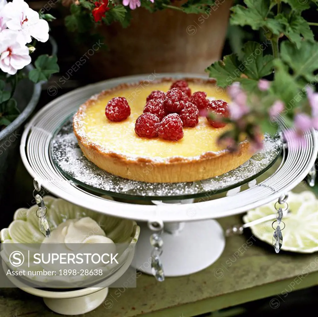Lemon tart topped with raspberries on a serving plate.