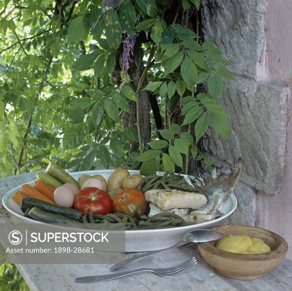 Large white bowl filled with vegetables, fish and eggs, wooden bowl with sauce on wooden table