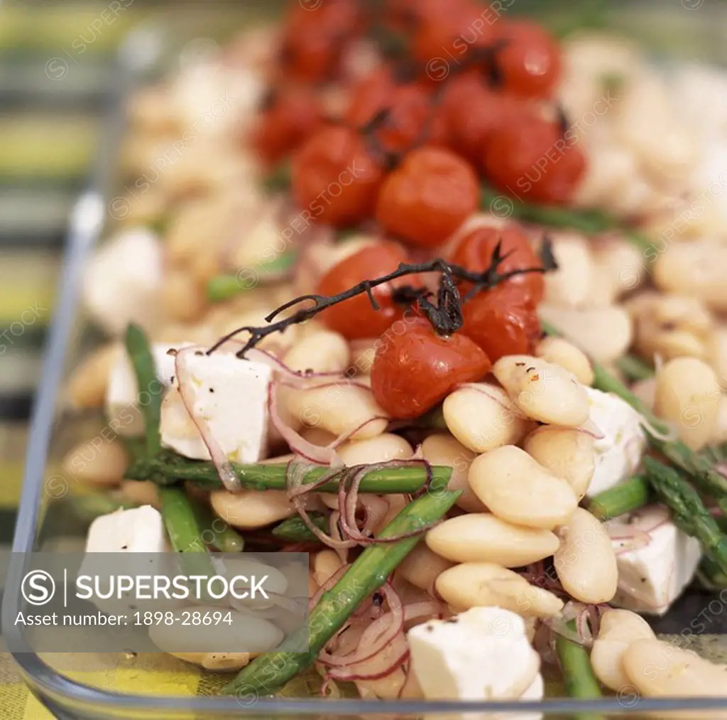 Fresh salad of butter beans, tomatoes, feta cheese, and asparagus on a glass platter.