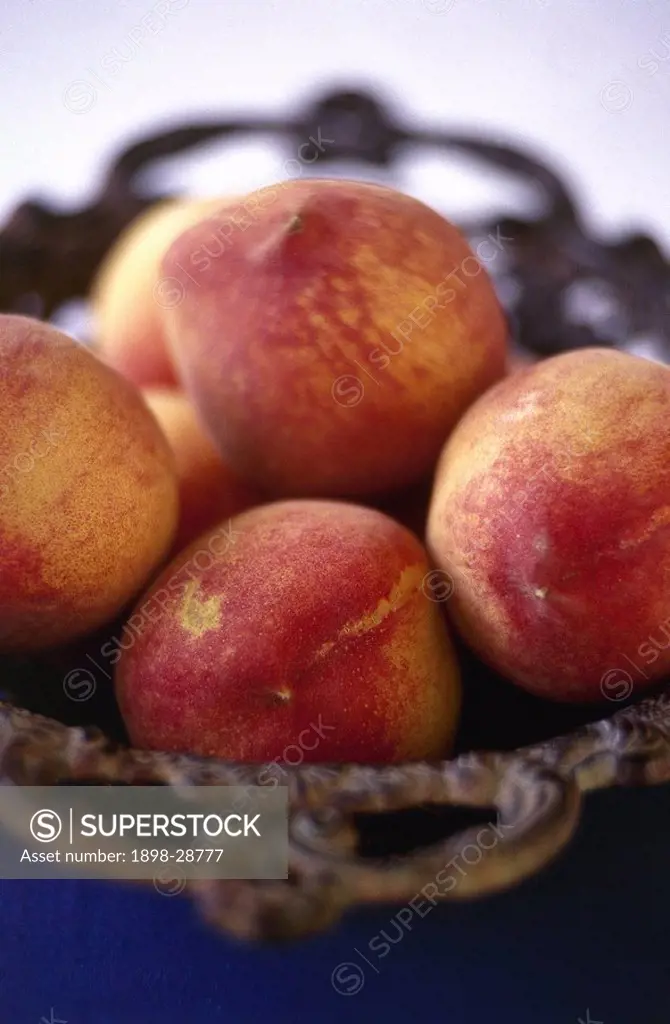 Ripe peaches in a decorative, wrought iron fruit bowl.