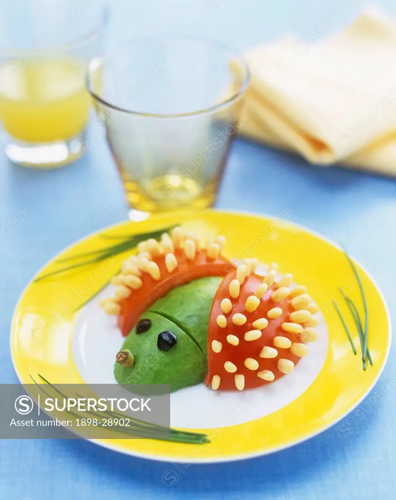Close up detail of a novelty meal with avocado and tomatoes in the shape of a small animal on a yellow plate.