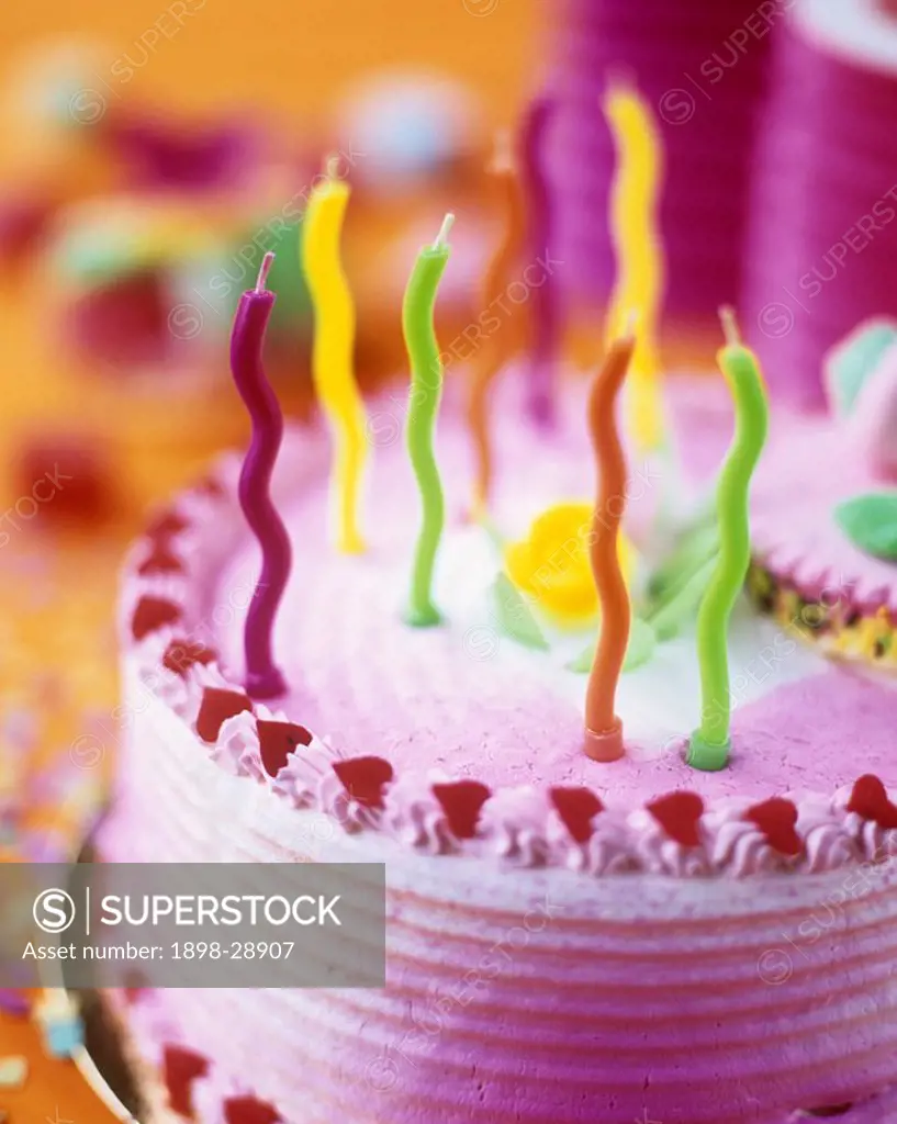 Close up details of a colourful birthday cake with colourful wavy candles.