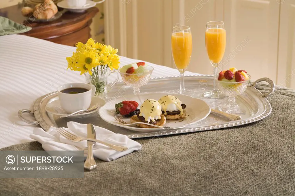 Eggs benedict and orange juice on silver tray on bed