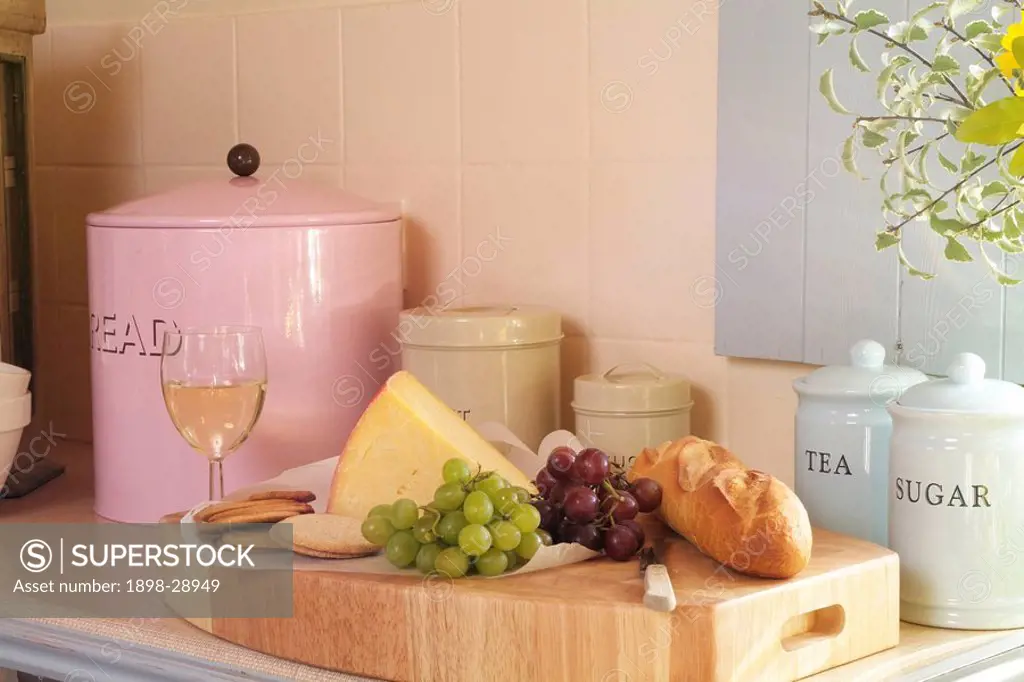 Chopping board with bread and cheese next to grapes and a glass of wine