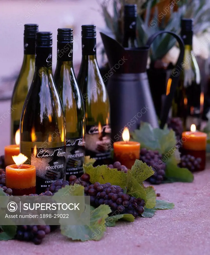 Wine bottles with lit candles and grapes on the centre of a table.