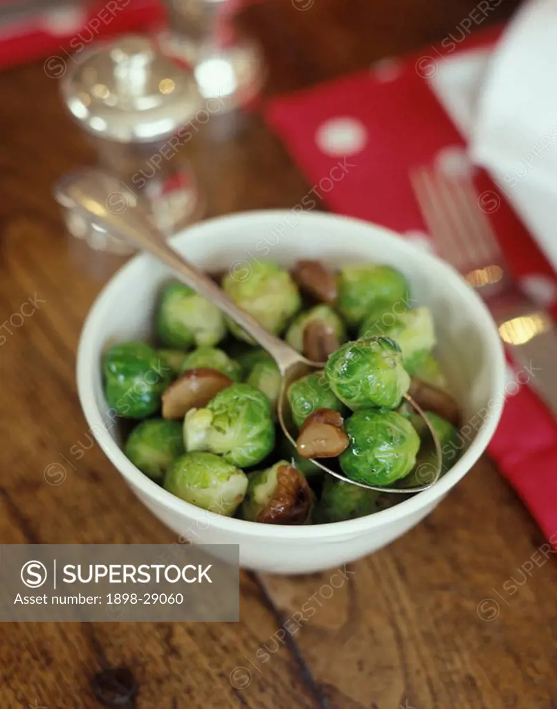 Bowl of brussel sprouts and walnuts with silver serving spoon on wooden table.