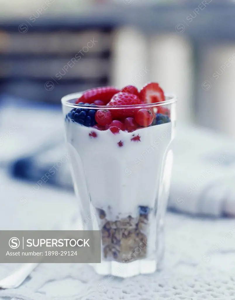 Close up of a fruit sundae in a glass on a lace tablecloth.