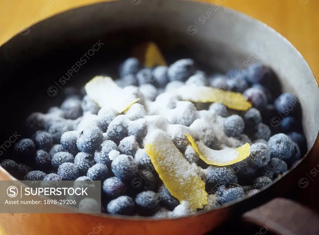 Cooking pot filled with fresh blueberries coated with sugar and lemon rind
