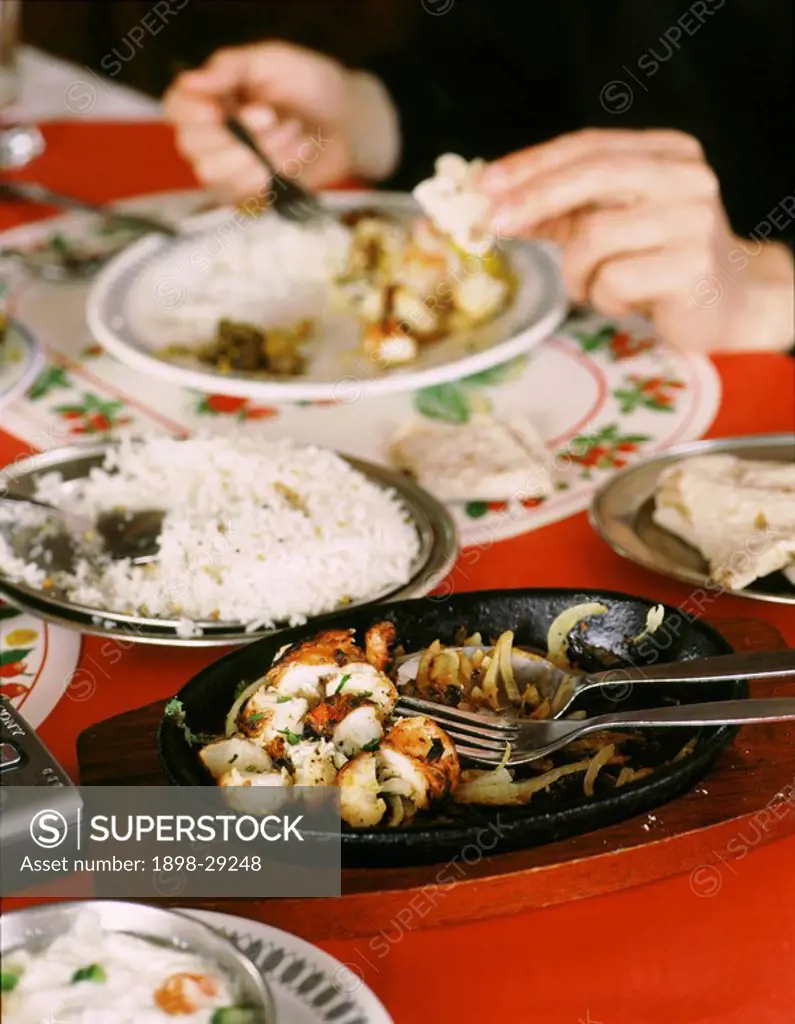 Person eating in Indian restaurant at table laid with chicken tikka, white rice and chapatti