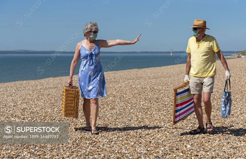 South sea, Portsmouth, Southern England, UK, Woman wearing a surgical mask social distancing from her husband during the Corvid-19 outbreak On the beach in South sea, UK