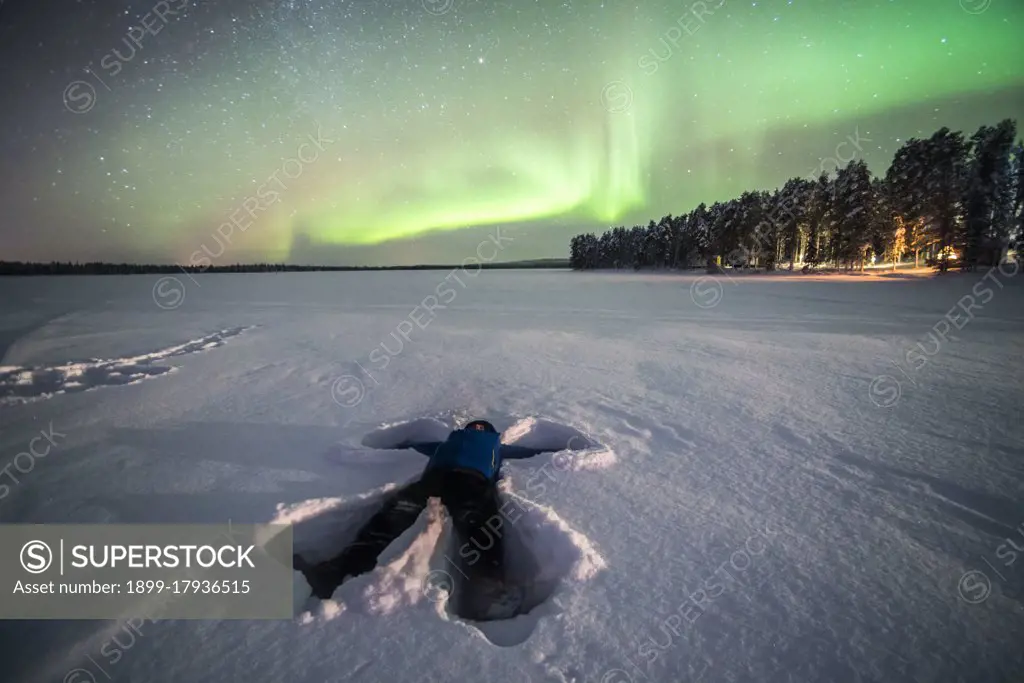 Person under Northern Lights, aurora borealis, display of bright colorful green and purple in remote winter snow covered lake landscape scenery in Finnish Lapland, inside Arctic Circle in Finland