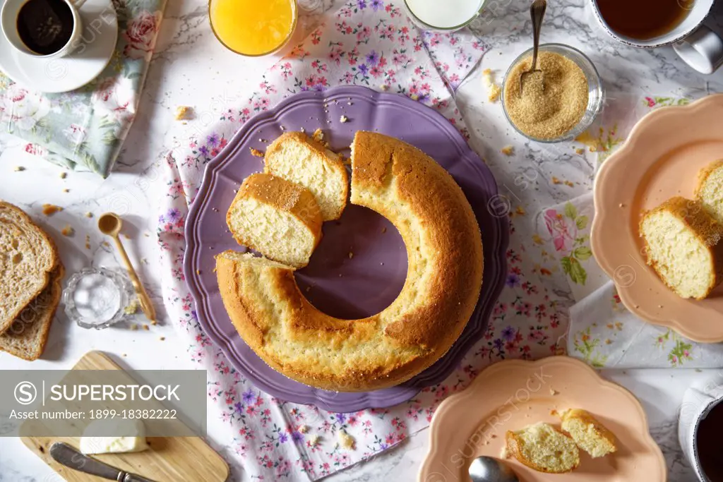 A breakfast marble table with sandwich bread, butter, salt, tea and coffee, orange juice and a ring shaped cake. coloured plates and roses napkin. top view. (Photo by: Costanza Sigismondi/REDA&CO/)
