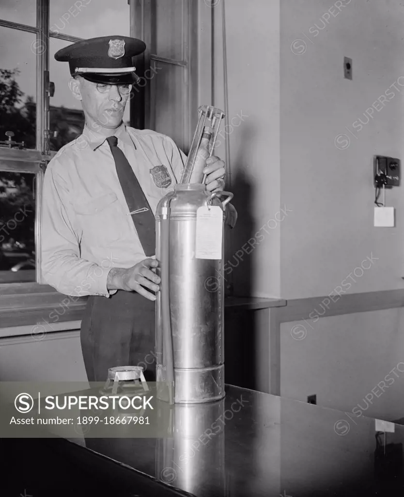 An officer in the Justice Department Guards, examines a new type of fire extinguisher cartridge, the cartridge is filled with carbon dioxide gas circa 1937.