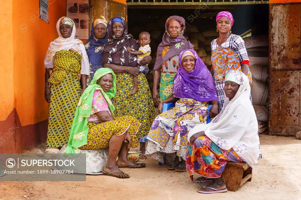 These West African women wearing traditional colorful dress pose for the camera in their village ca. 21 February 2018.