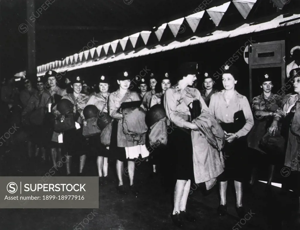 A group of female military nurses in uniform stands in rows at an unidentified location. 