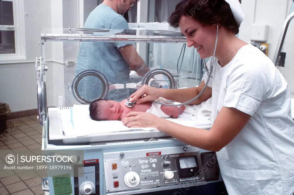 1977 - A nurse examines an infant in an incubator. 