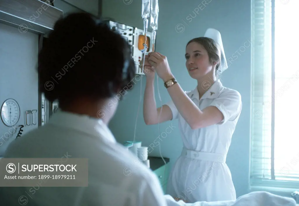 1975 - A nurse adjusts the flow of an intravenous solution. 