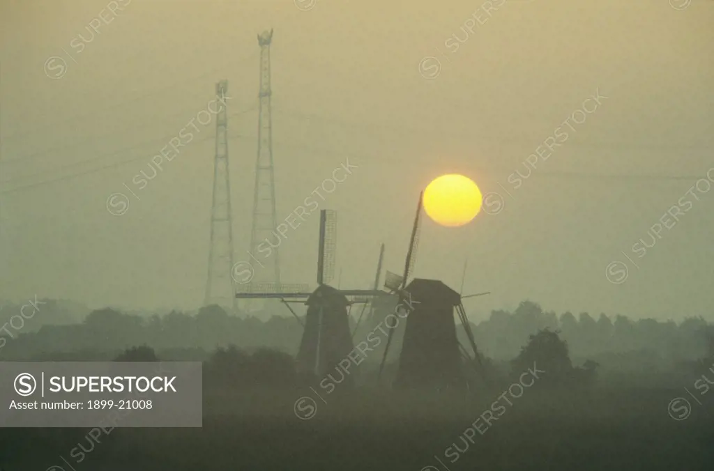 Windmills & electricity pylons at sunset, Holland. 