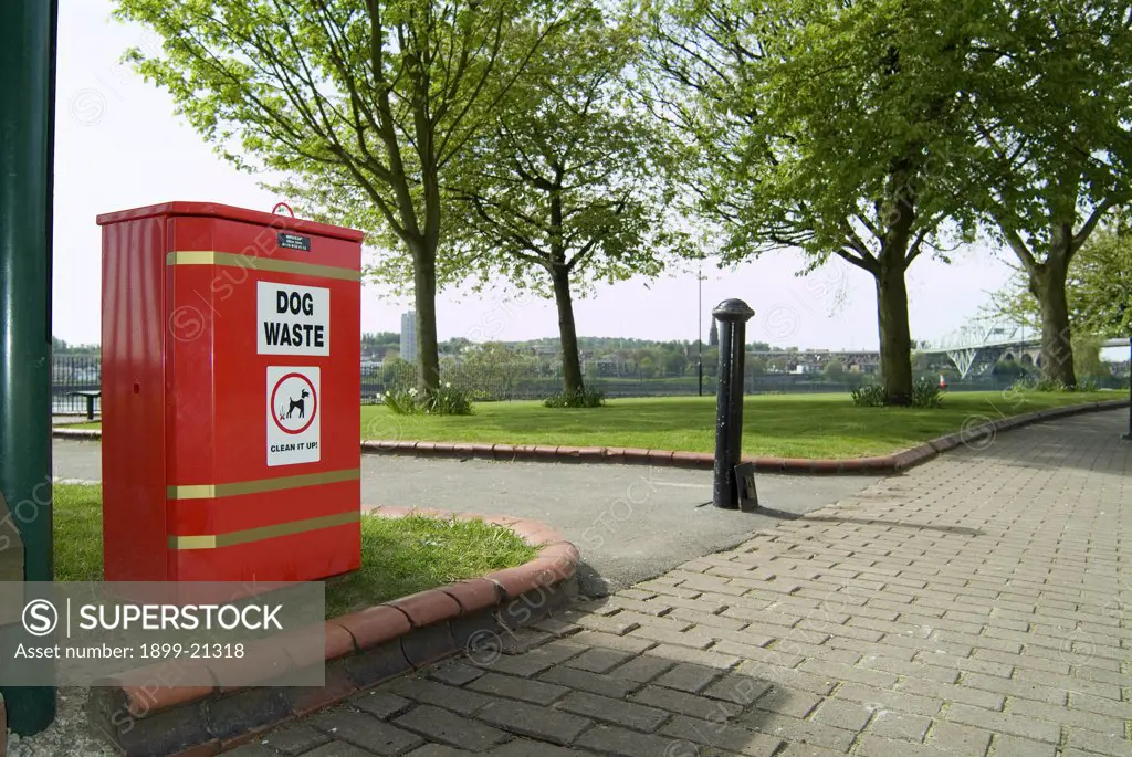 Dog waste bin, United Kingdom. Red dog waste bin - for responsible dog owners to deposit their pets excrement, adjacent to childrens playground and leisure park by the banks of the River Mersey in West Bank, Widnes, Cheshire.