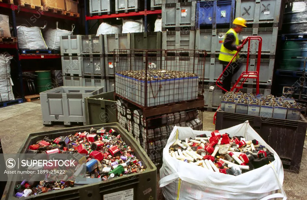Collecting batteries for recycling, United Kingdom. Collecting batteries for recycling. Large containers and shelves with batteries of all sizes. Man wearing yellow hard hat standing on portable steps. Batteries contaminate ground if dumped and chemicals allowed to leak out - nickel cadnium, zinc. If recycled, metals are reclaimed and re-used.