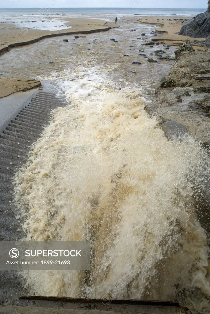 Storm drain discharging water onto beach after prolonged heavy rainfall, Caswell Bay, Gower, Wales, United Kingdom. 